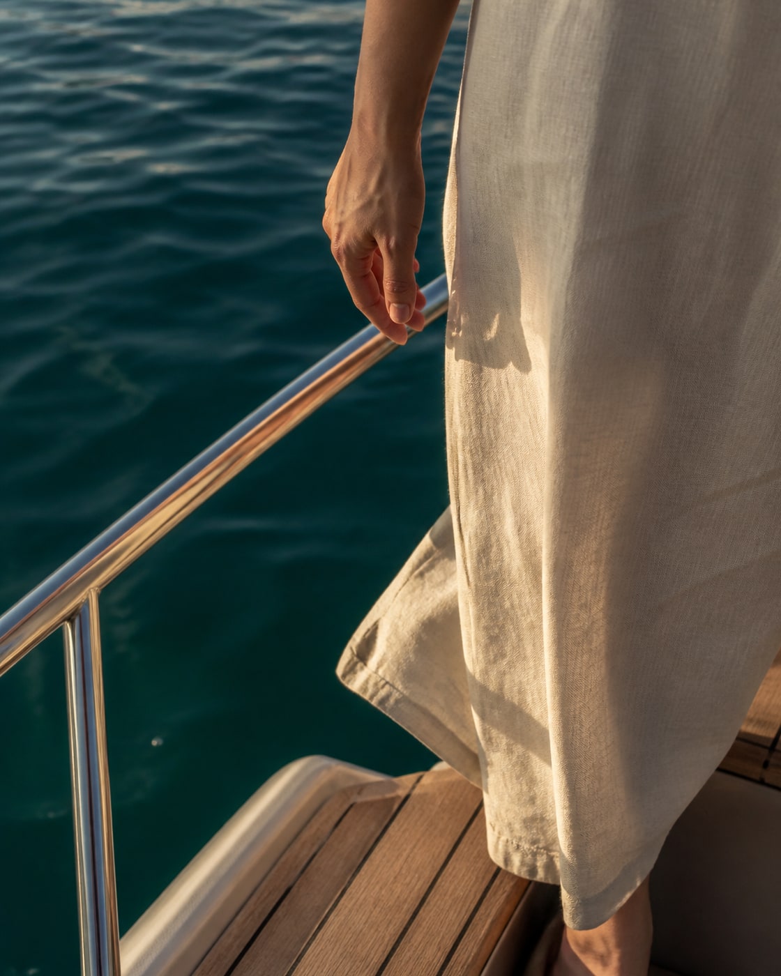 Anonymous fictional guest boarding beside deep teal water in warm evening light